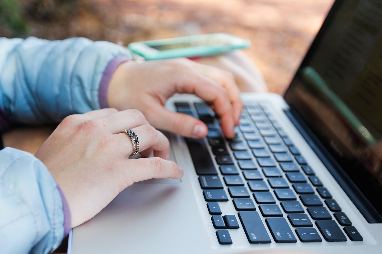 Close up of girl's hands as she types on a computer next to her cell phone
