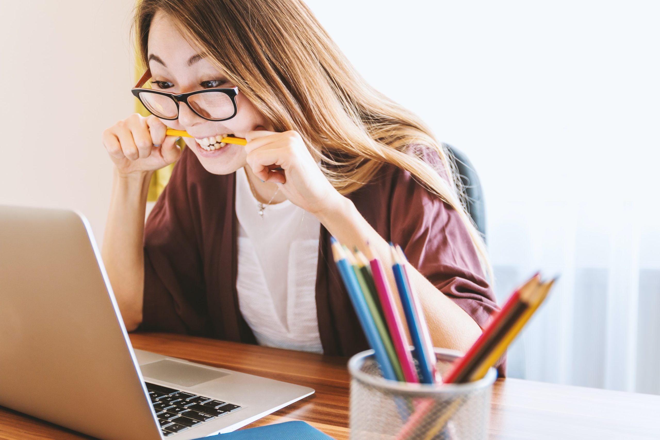 a girl in glasses frustrated while staring at her laptop biting a pencil